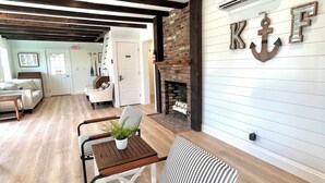 Un salon chaleureux avec une cheminée, un canapé à rayures, un plancher en bois et des poutres apparentes.