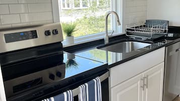 Una cocina moderna con un extractor de acero inoxidable, horno empotrado, un lavamanos doble y una ventana con vistas al exterior.