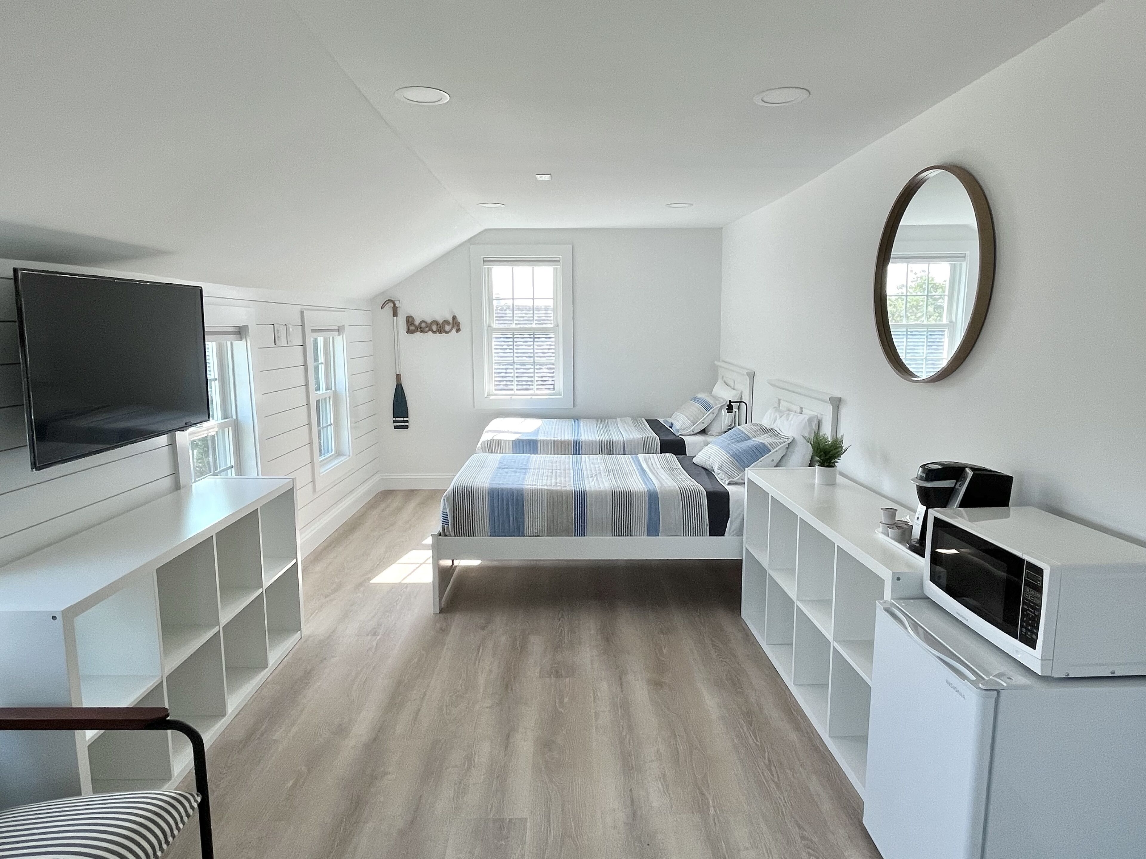 Un dormitorio moderno con televisión, dos camas, cómoda y microondas.