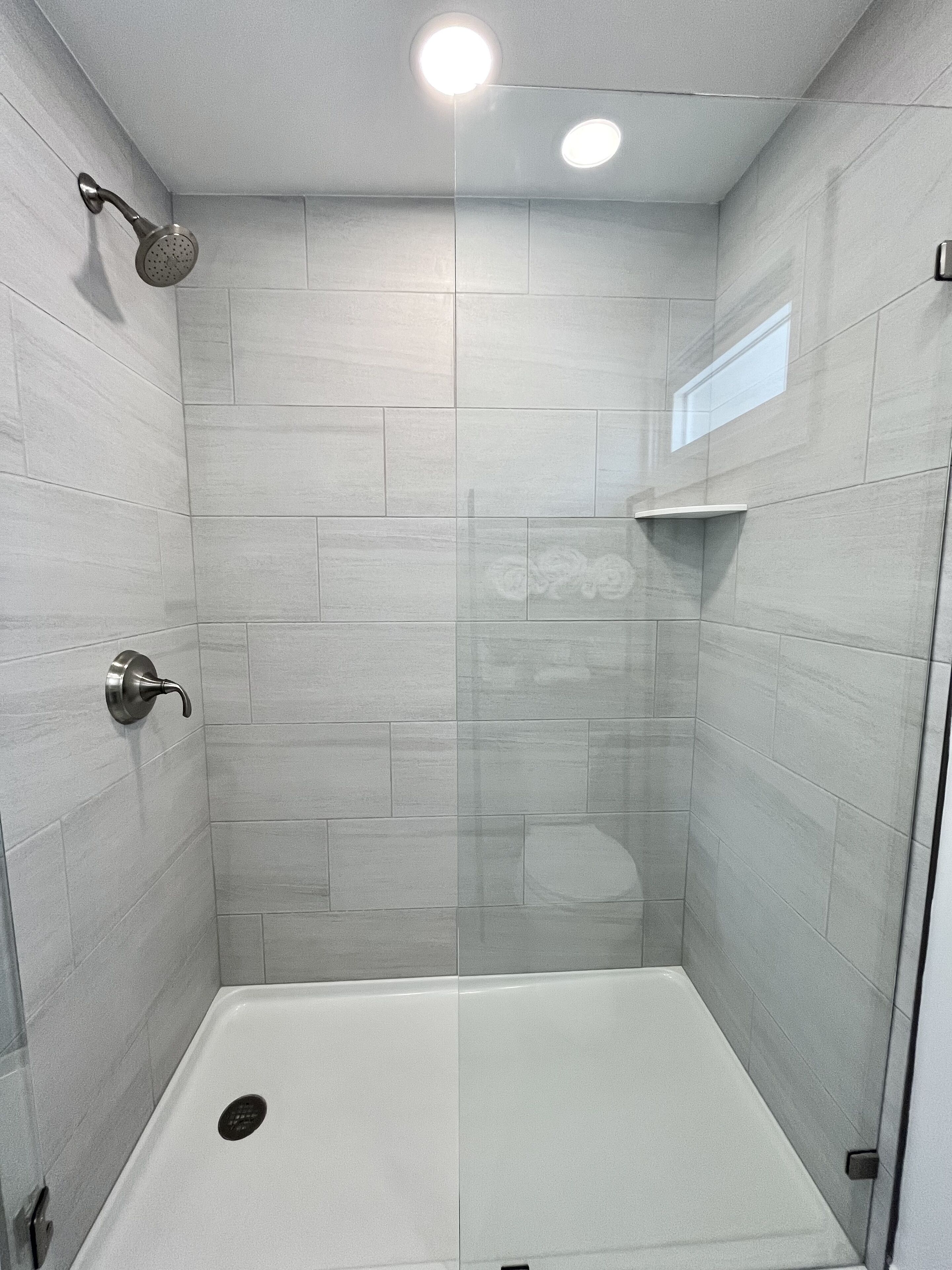 Una ducha moderna con puerta de vidrio, cabezal de ducha de mano y control en la pared.