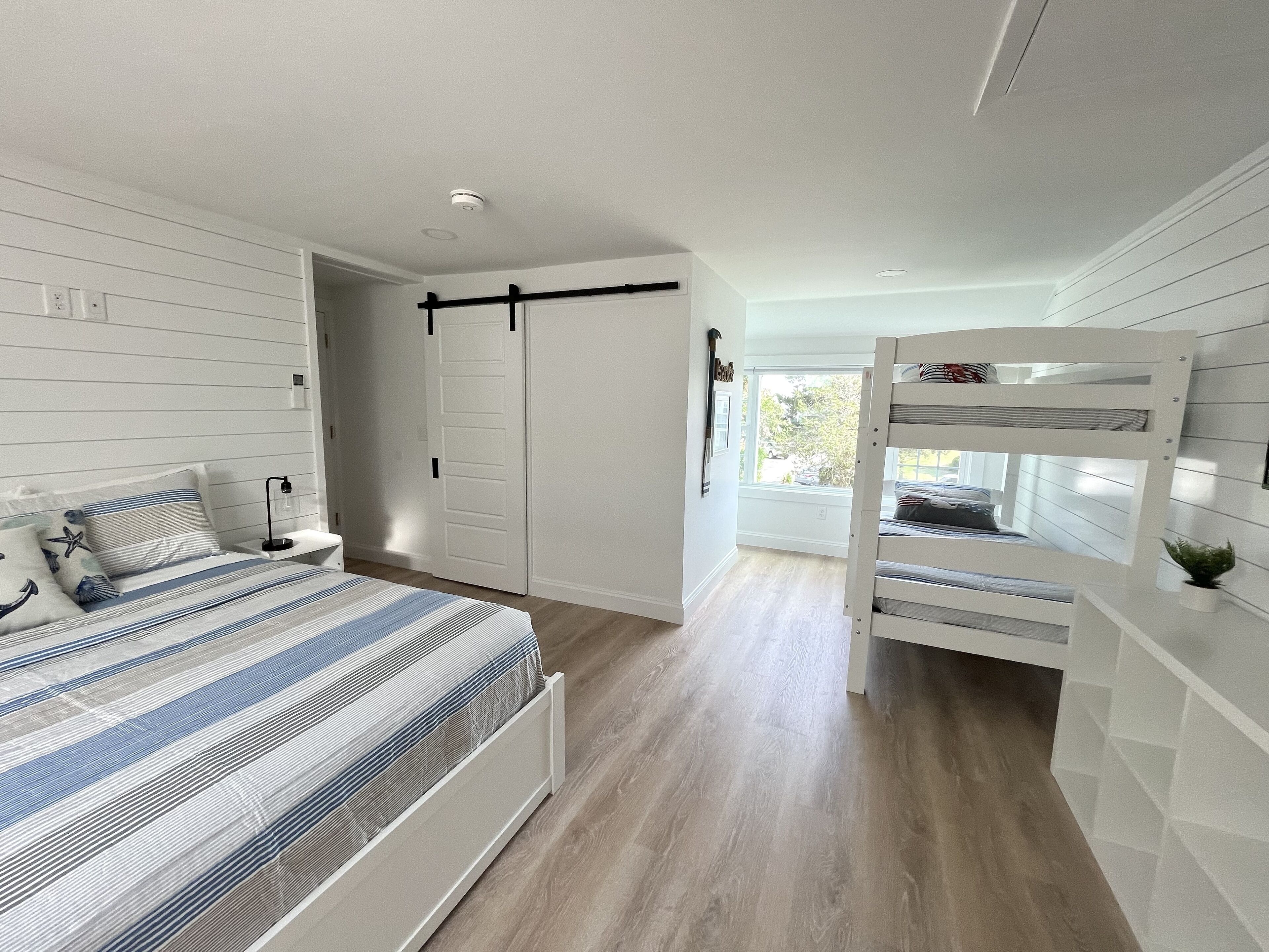 Quarto com cama, mesa de cabeceira e beliche.