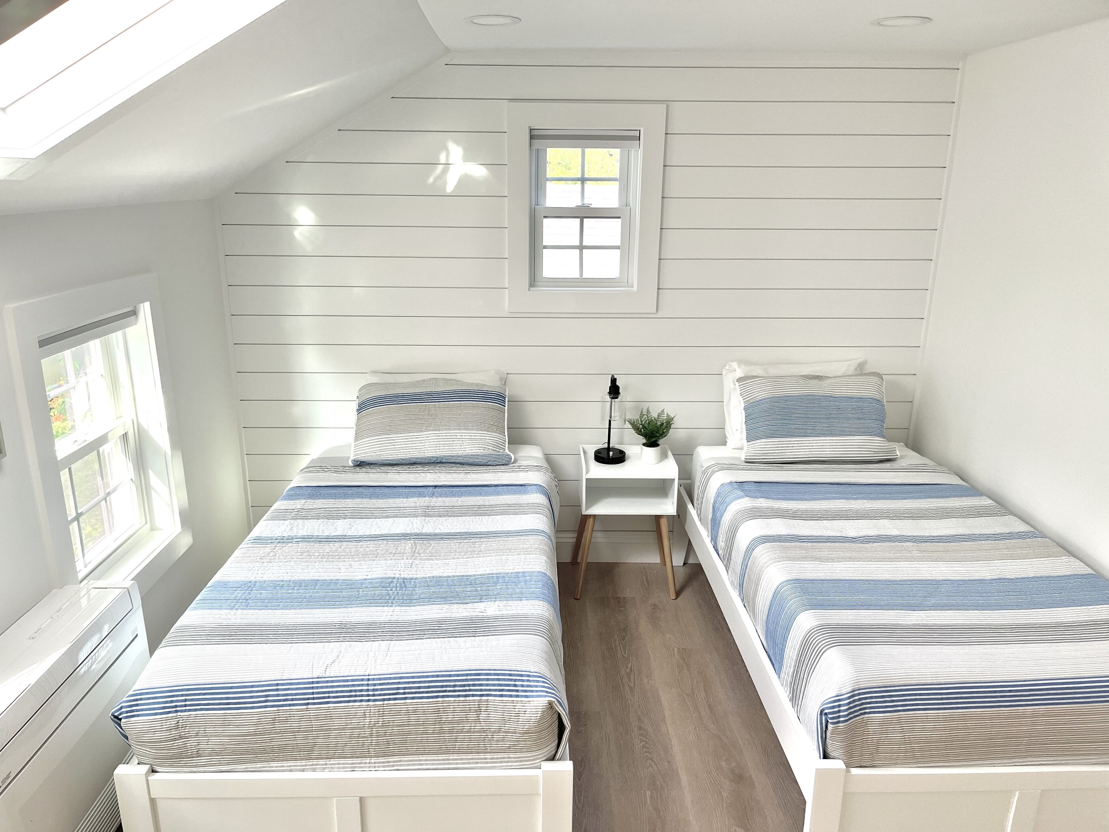 A bedroom with two beds, a small bedside table, a window, and a skylight.