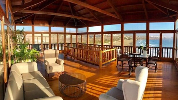 A spacious indoor area with wooden flooring, a high ceiling, and large windows offering ocean views. There are several seating areas with chairs and a table. - El Mirador de Fuerteventura (Puerto del Rosario)