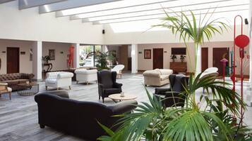 A spacious lobby with multiple seating areas, including sofas and armchairs, arranged around a central coffee table.
