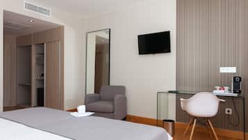 A hotel room with a bed, a chair, a desk with a computer, a TV, and a wardrobe.