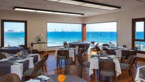A restaurant with multiple tables set for dining, large windows offering ocean views, and a modern interior design. - El Mirador de Fuerteventura (Puerto del Rosario)