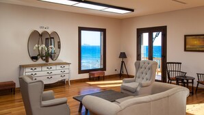 A living room with a sofa, two armchairs, a coffee table, a sideboard, and a large mirror. There are two windows with ocean views. - El Mirador de Fuerteventura (Puerto del Rosario)