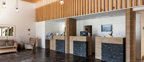 Un espace d’accueil avec un lambris en bois, un comptoir de réception, un ordinateur et un coin salon comprenant un canapé et des fauteuils.