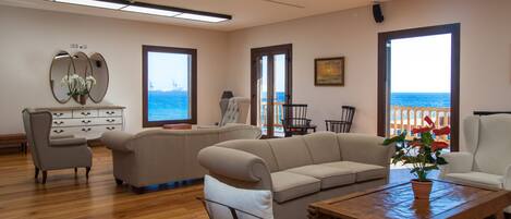 A spacious living room with a large sofa, a wooden coffee table, and a view of the sea through large windows.