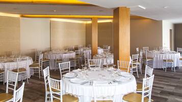 A banquet hall with round tables set for dining, white chairs, and a polished wooden floor.