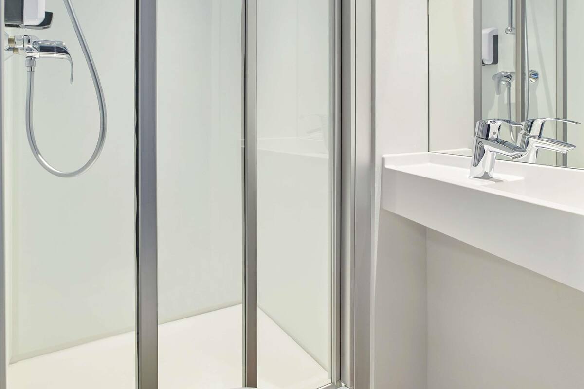 Une salle de bain moderne avec une douche à parois de verre, un lavabo blanc et un miroir.