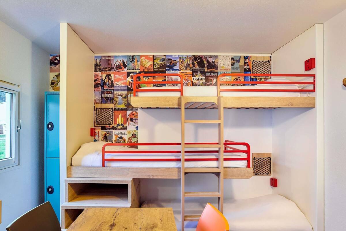 Une chambre avec un lit superposé, un mur recouvert d’affiches de voyage, un bureau et une chaise.