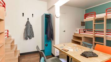 A room with bunk beds, a table with playing cards, a chair, and a coat rack.