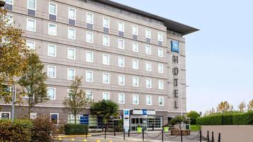 A multi-story hotel with a flat facade, a prominent 'HOTEL' sign, and a parking area with yellow bollards.