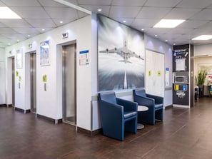 A modern waiting area with elevators, a large mural, and seating. - ibis budget Roissy CDG Paris Nord 2 (Roissy-en-France)