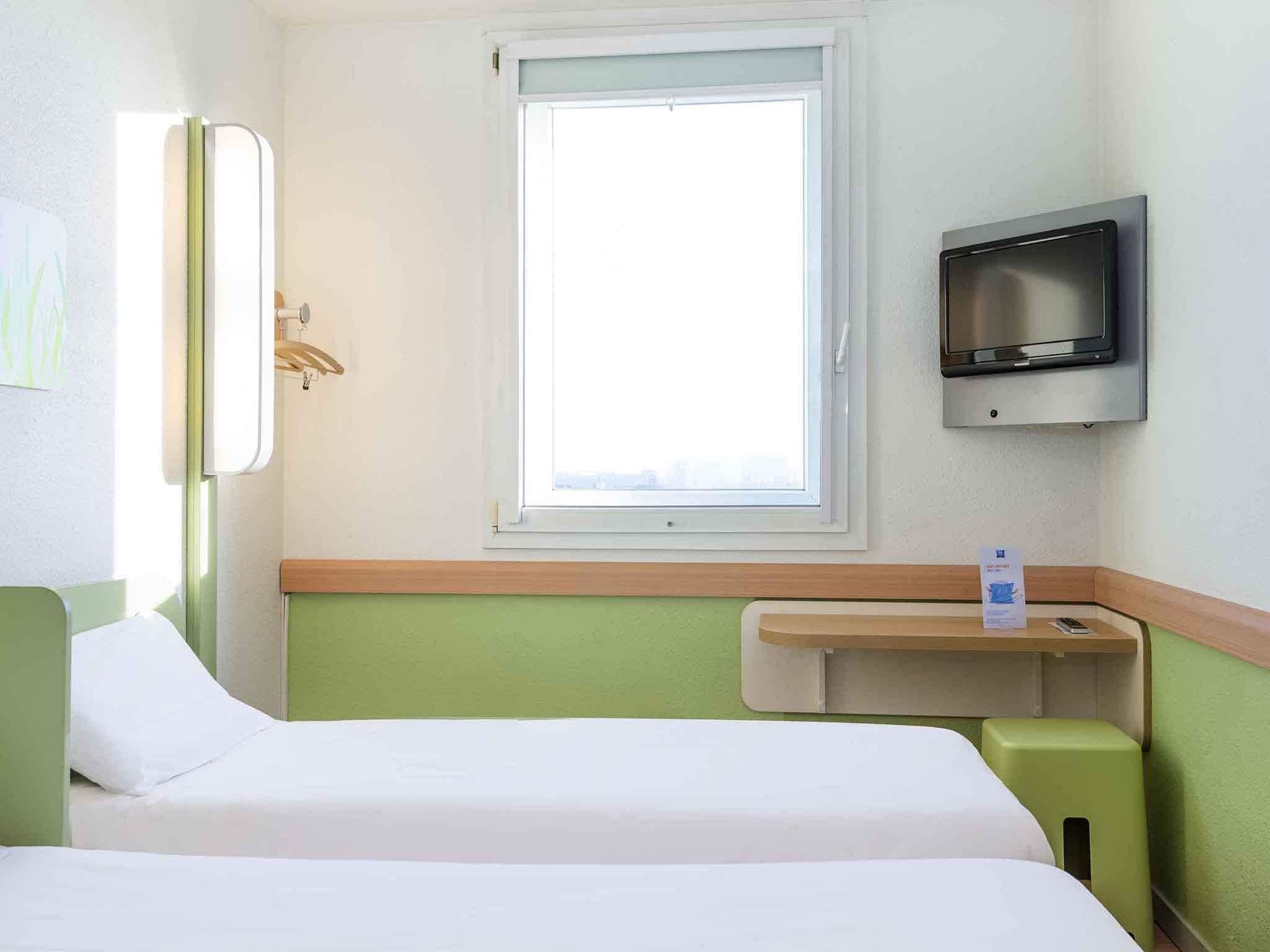 Una habitación de hotel con cama, televisión, ventana y una mesita.