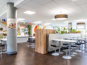 Interior de una cafetería moderna con una barra central, varias mesas y sillas, y un pilar decorativo.
