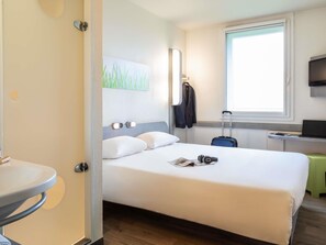 A hotel room with a bed, a desk with a laptop, a suitcase, and a coat rack. - ibis budget Roissy CDG Paris Nord 2 (Roissy-en-France)