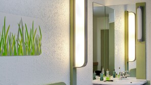 Een hotelkamer met een bed, een nachtkastje, een spiegel en een wastafel aan de muur.