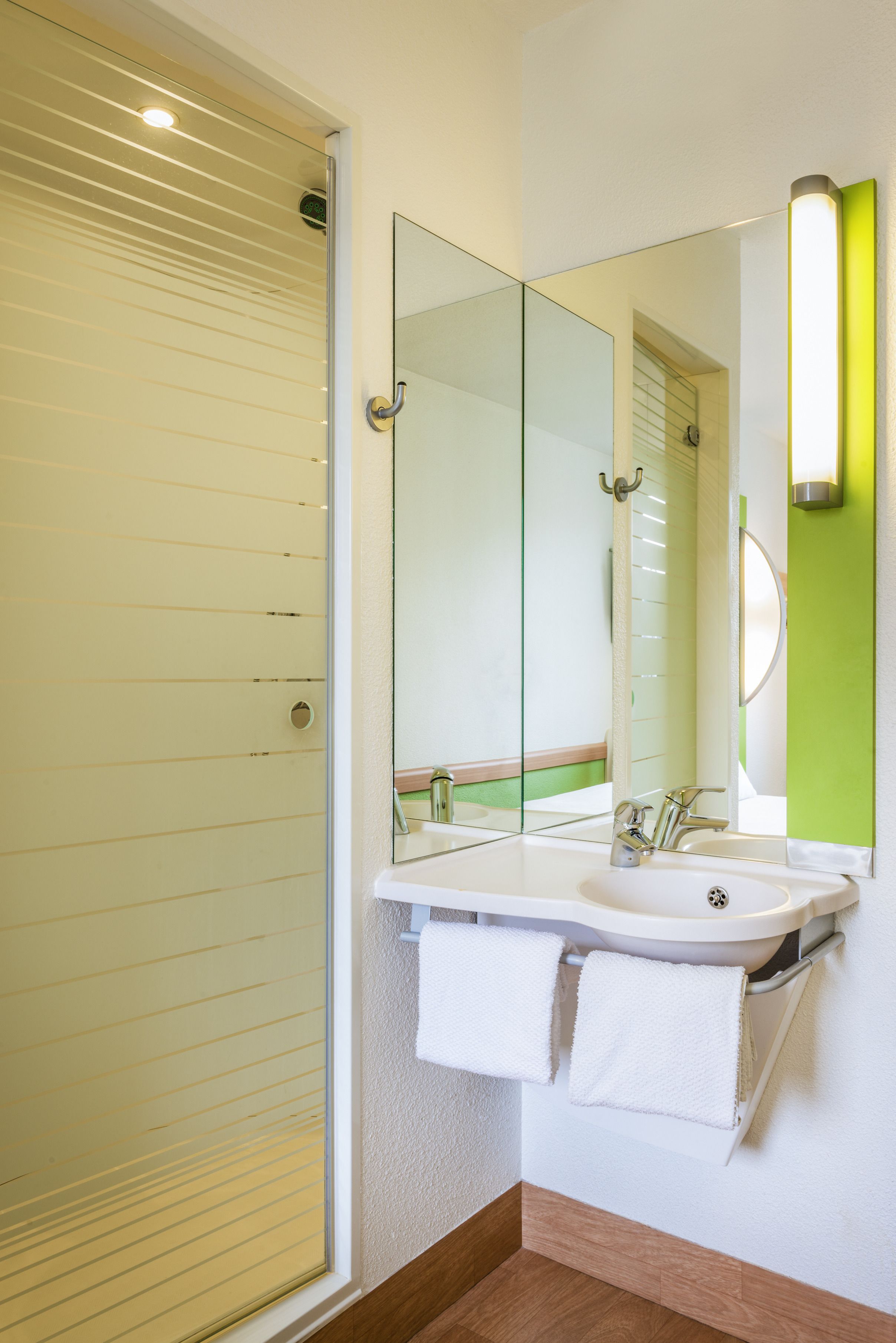 Een badkamer met een glazen douchedeur, een witte wastafel met een spiegel erboven en een groene accentmuur.