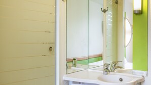 Een badkamer met een glazen douchedeur, een witte wastafel met een spiegel erboven en een groene accentmuur.