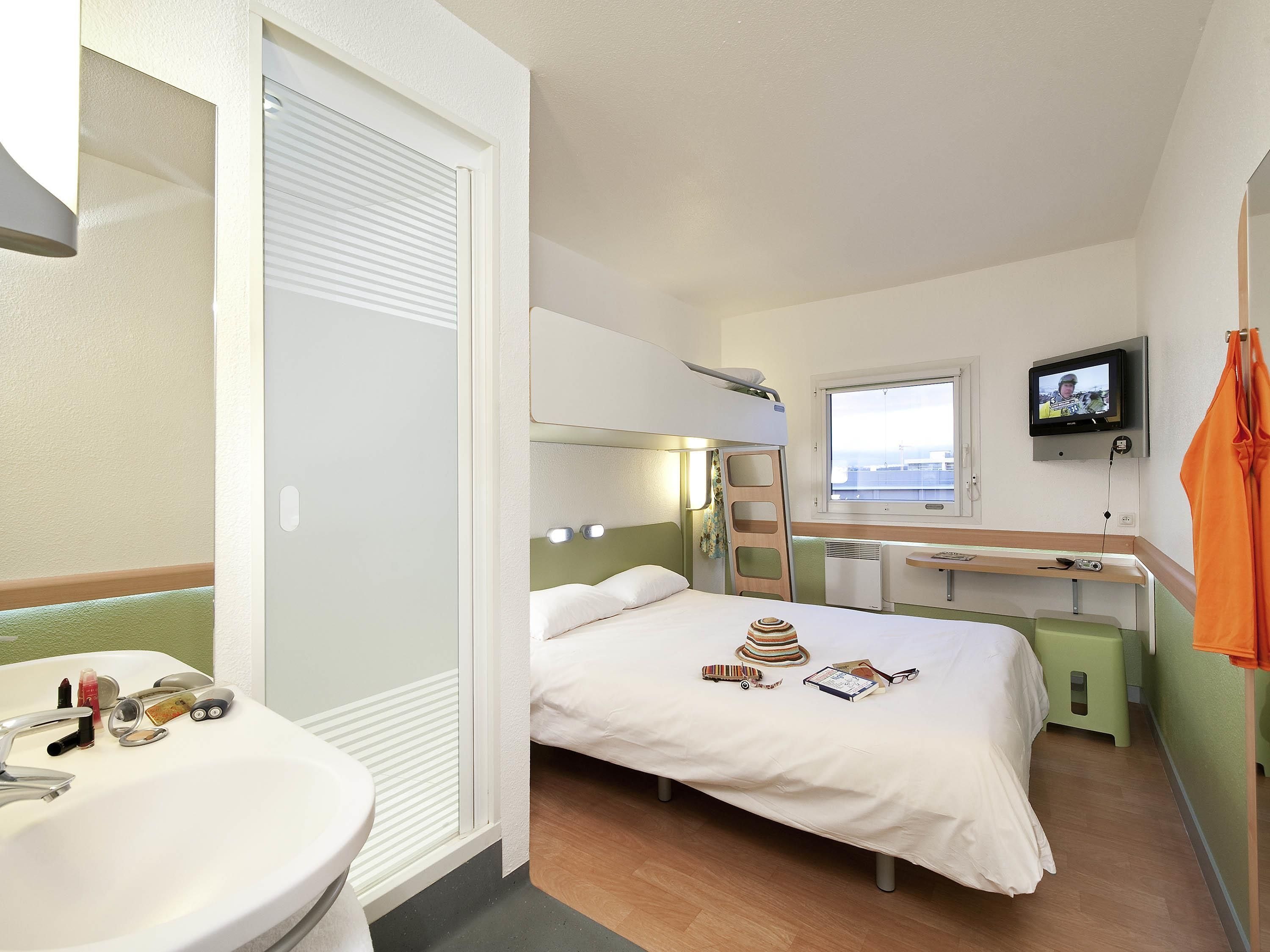 Ett hotellrum med en säng, en tv, ett fönster, ett handfat och en spegel.