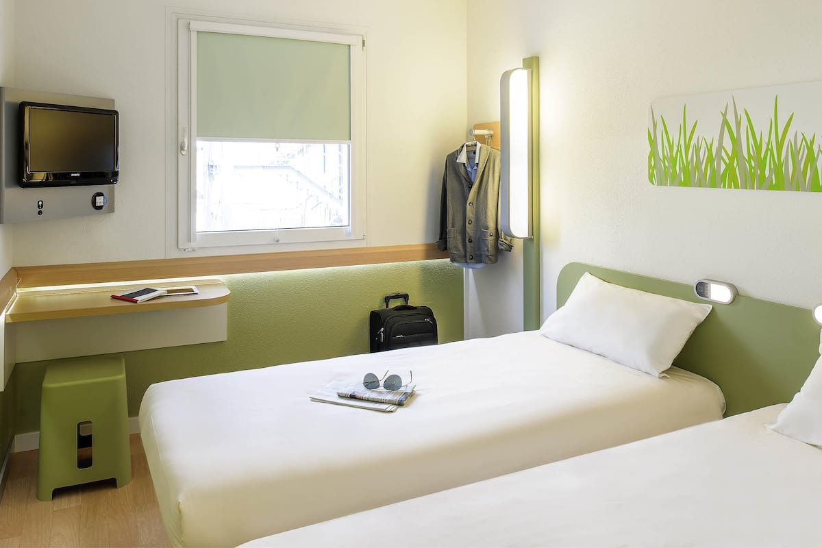 Une chambre d’hôtel avec un lit, un bureau équipé d’un ordinateur, une fenêtre et un téléviseur fixé au mur.