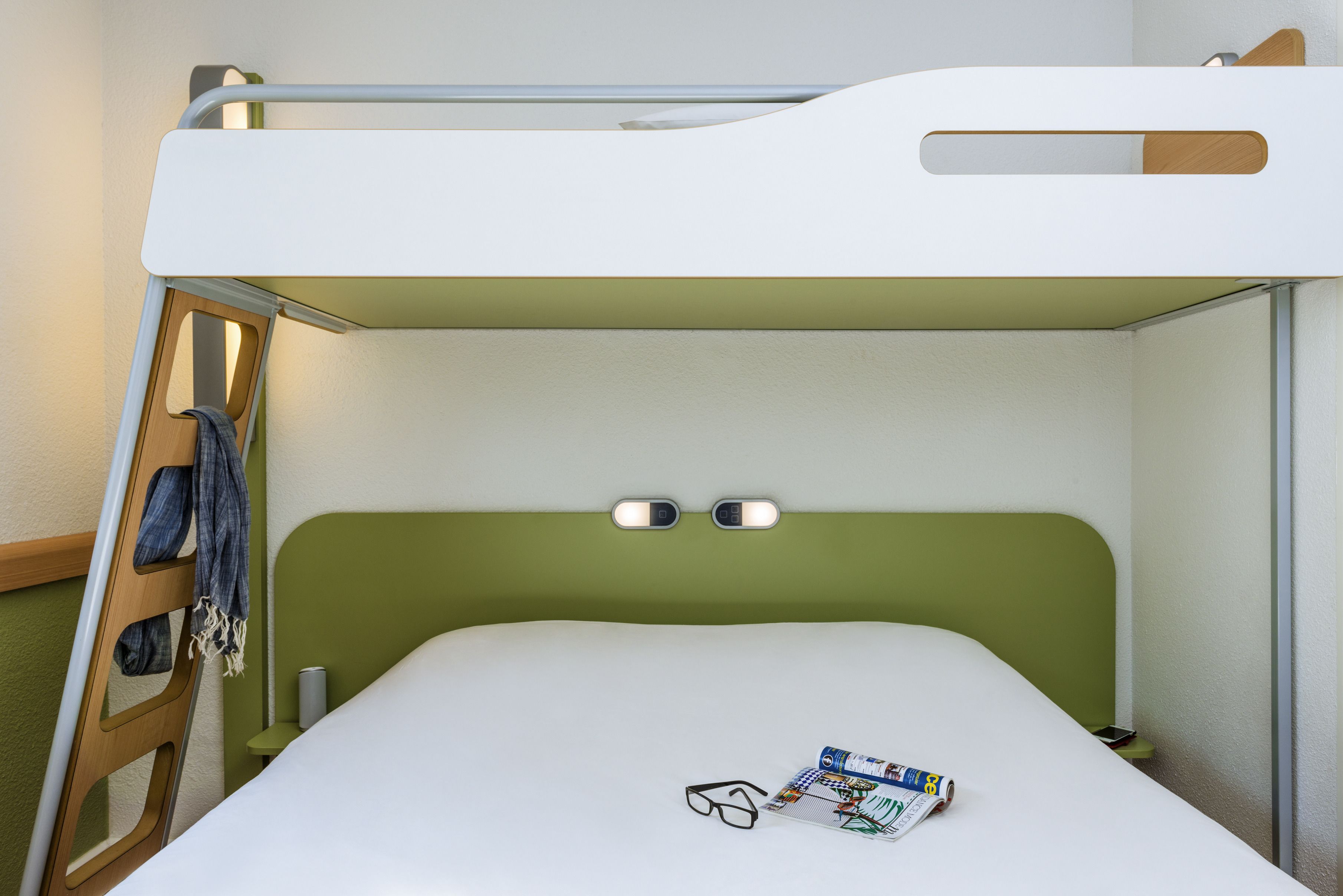 Un lit superposé avec une tête de lit verte, une paire de lunettes et un magazine sur le lit du bas.