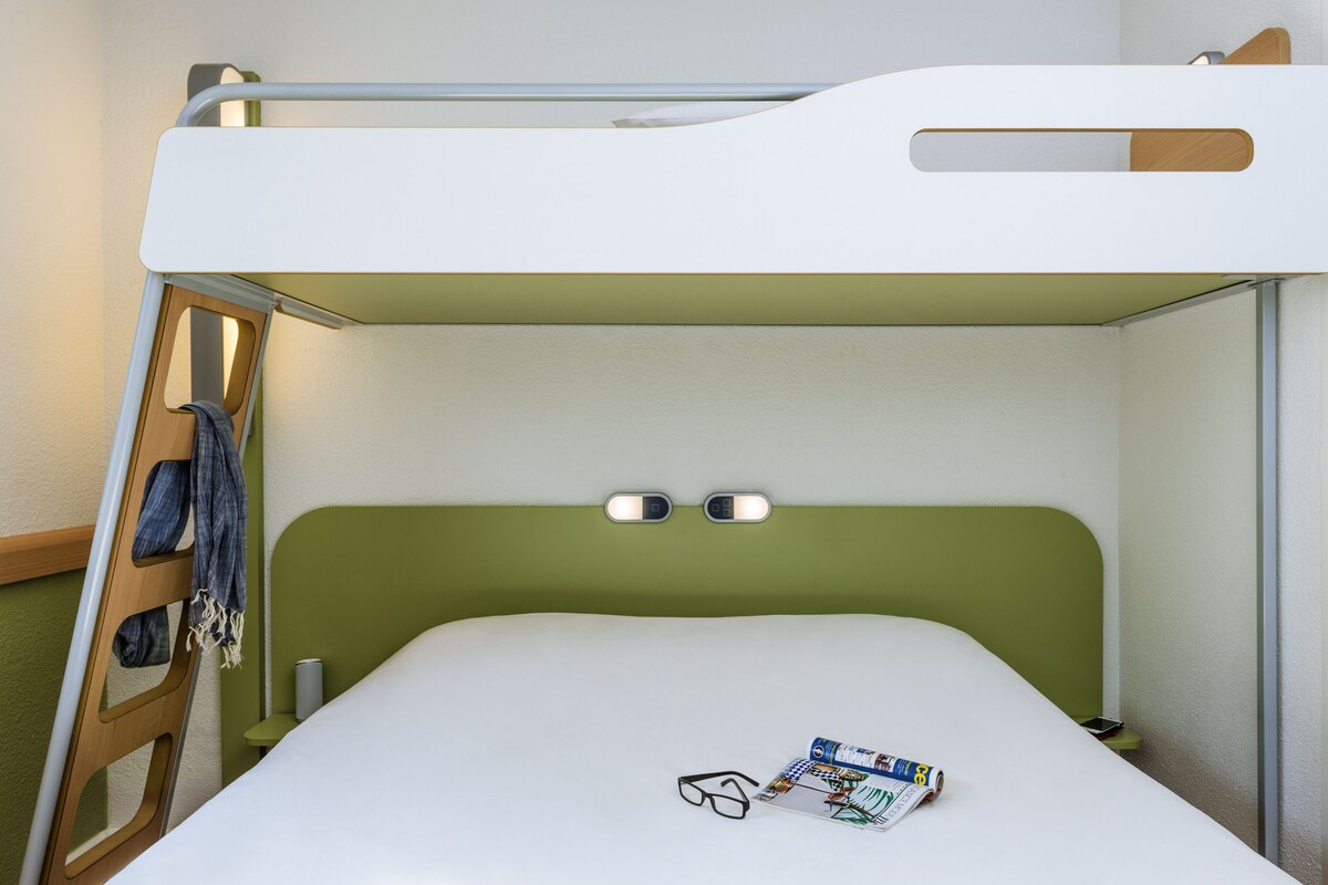 Ein Stockbett mit grünem Kopfteil, eine Brille und eine Zeitschrift auf dem unteren Bett.