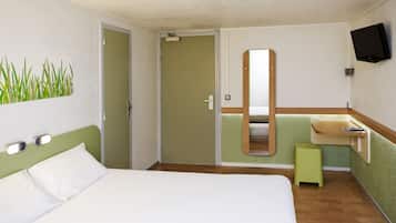 A hotel room with a bed, a green wall, a mirror, a TV, and a small stool.