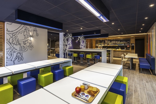 Un restaurante moderno con largas mesas compartidas, asientos coloridos y una zona de bar.