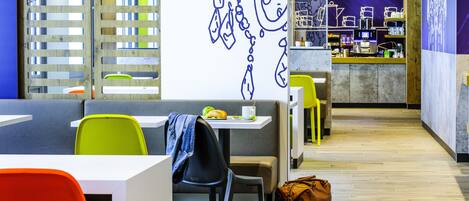 Un café moderno con arreglos de asientos, una barra con máquina de café y una pared decorativa.