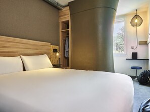 Une chambre d’hôtel avec un grand lit, une tête de lit en bois, une armoire intégrée, un luminaire suspendu et une fenêtre donnant sur un beau paysage.