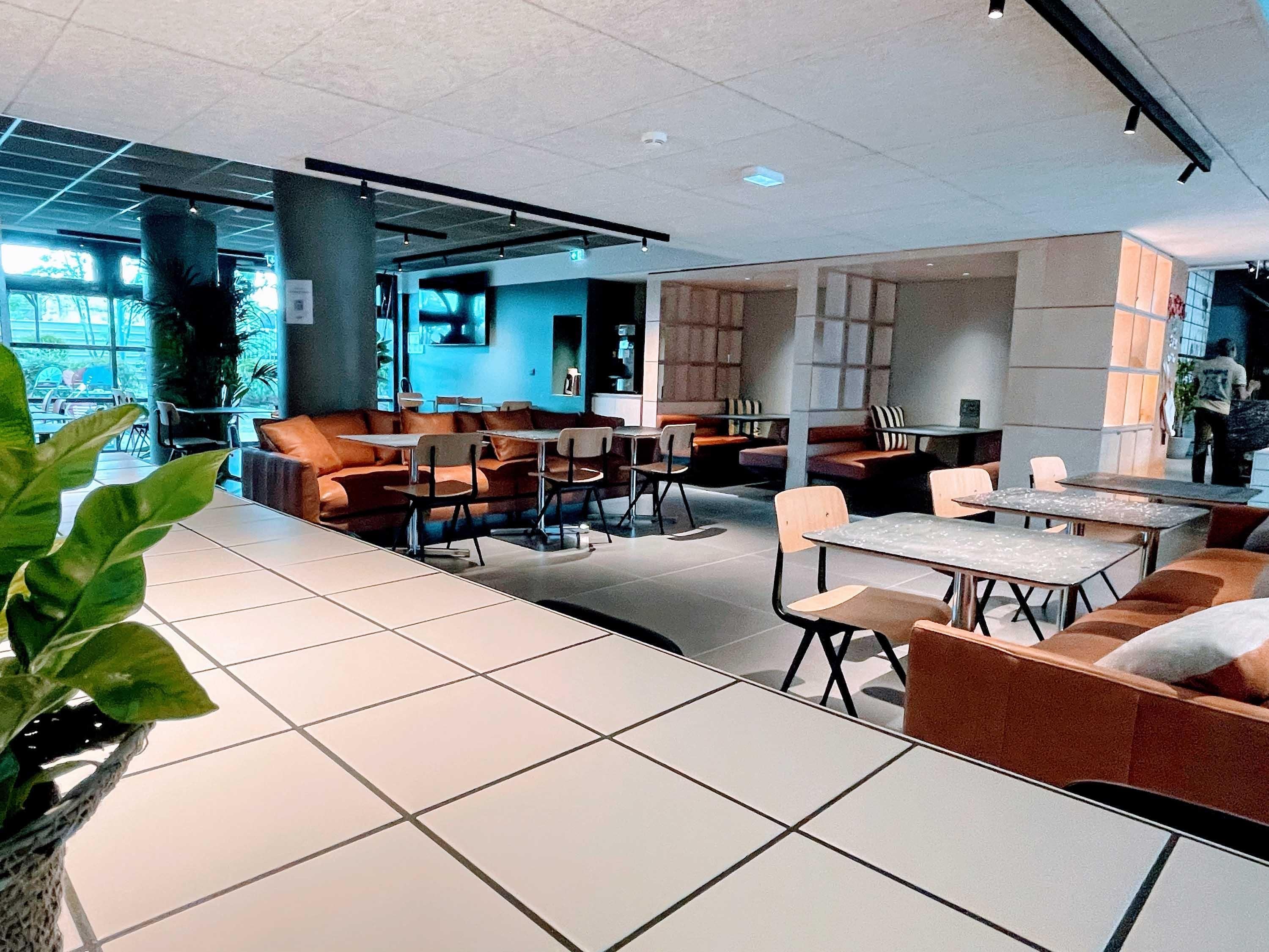 Un espace intérieur moderne doté de coins salon, de tables et d’une grande fenêtre laissant entrer la lumière naturelle.