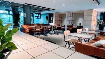 Un espace intérieur moderne doté de coins salon, de tables et d’une grande fenêtre laissant entrer la lumière naturelle.