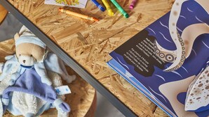 Une surface en bois avec un ours en peluche, des crayons de couleur et un livre.