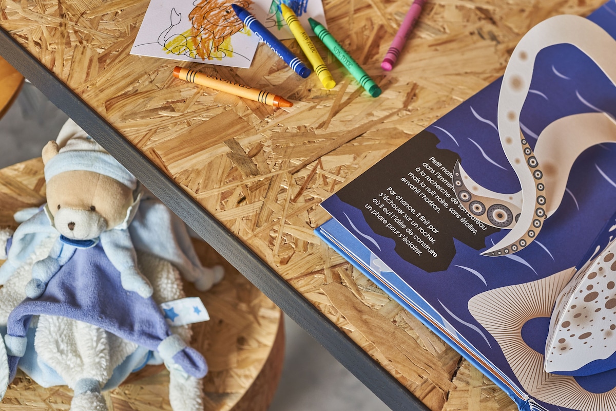 Een houten tafel met een teddybeer, kleurpotloden en een boek.