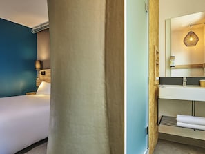 Hotelkamer met een bed, een wandlamp, een spiegel, een wastafel en een handdoekrek.