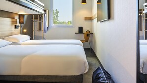 Une chambre d’hôtel avec deux lits, un bureau, une chaise, une télévision et une fenêtre donnant sur des arbres.