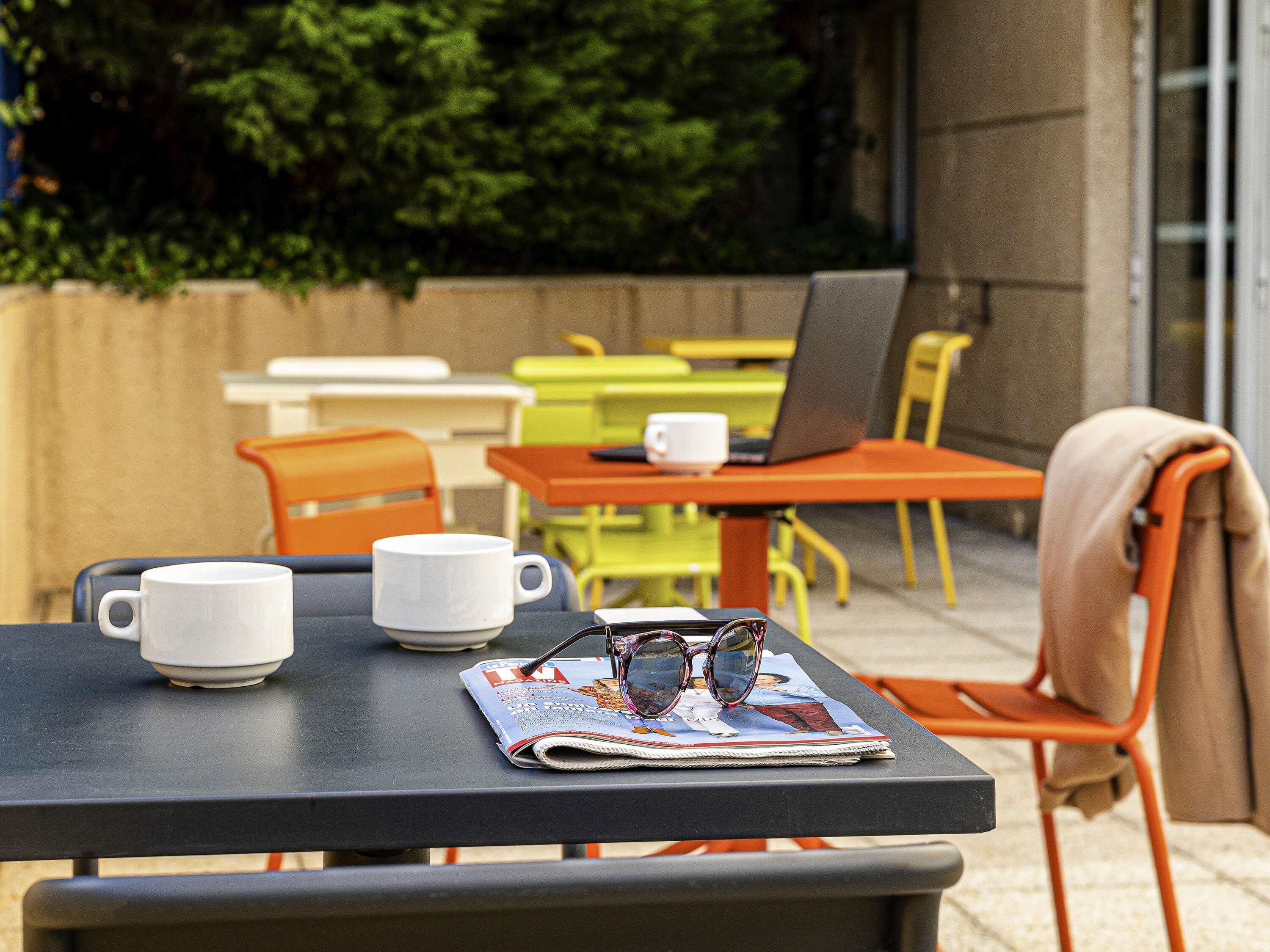 Une table avec un magazine, une paire de lunettes et deux tasses blanches.