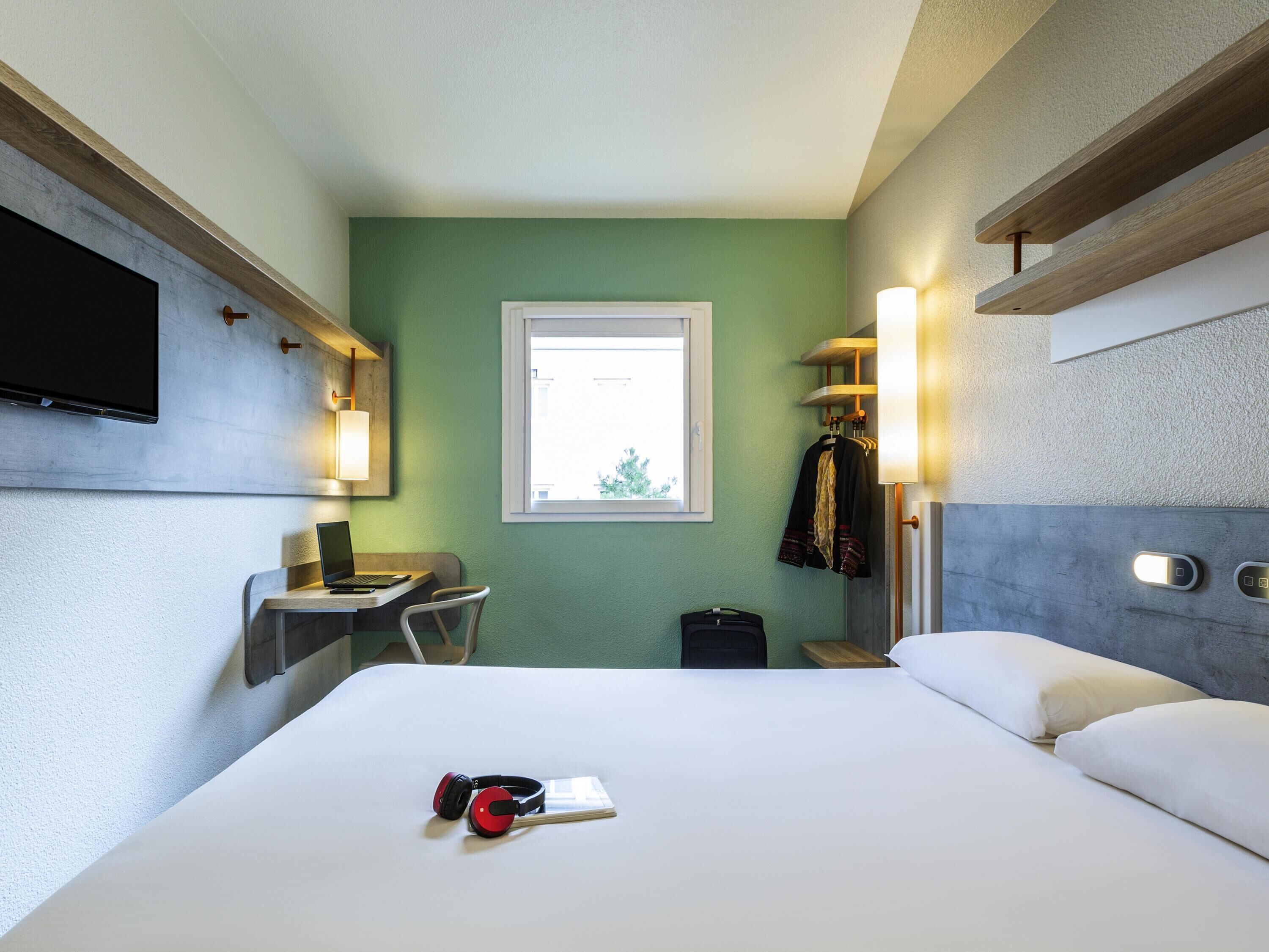 A hotel room with a bed, a desk, a chair, a TV, and a window.