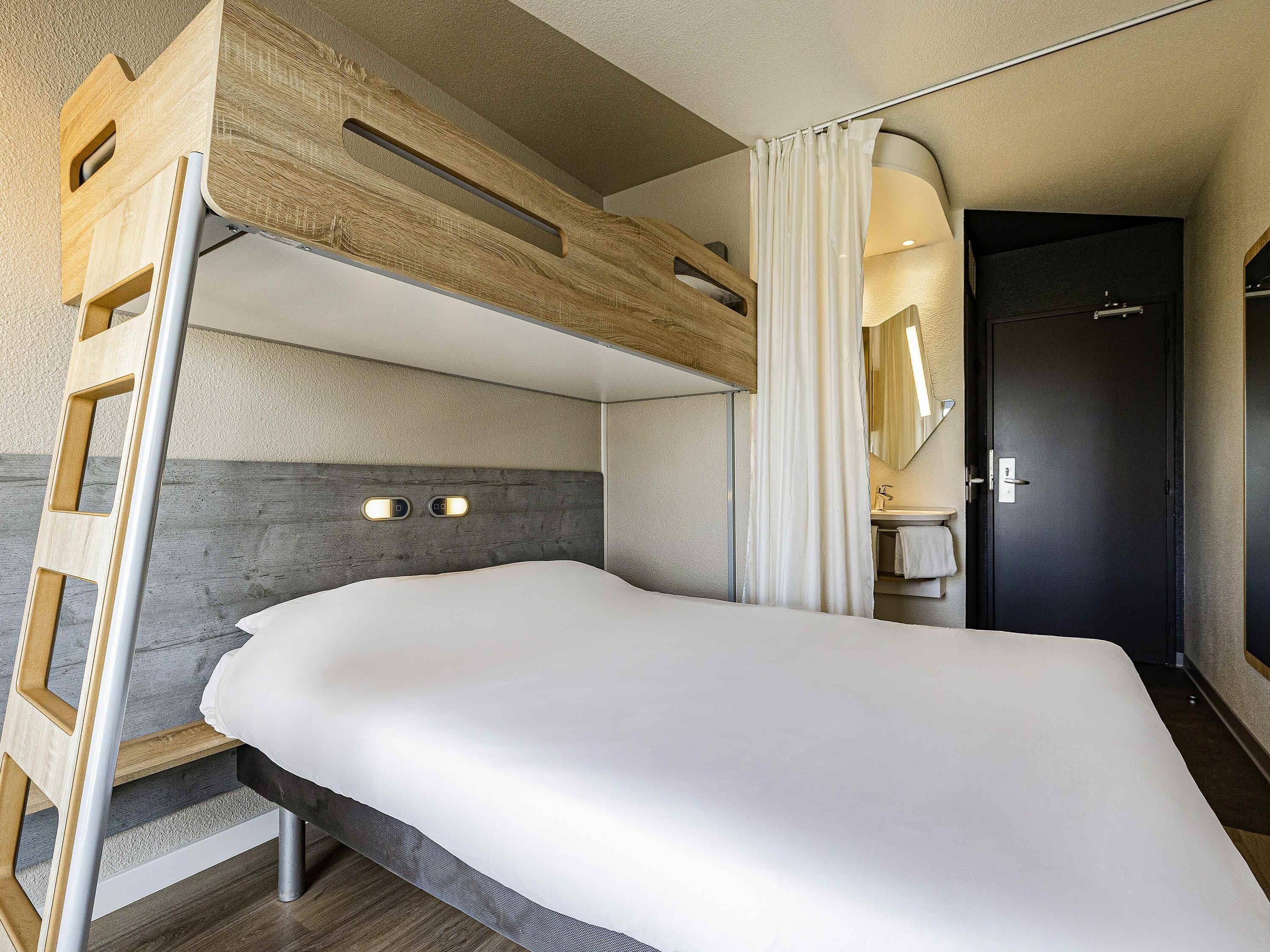 Una cama litera con escalera, una mesita de noche, un espejo y un baño con lavabo y toallero.