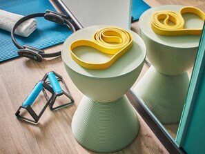 Ein Badezimmer mit einem grünen Hocker, einem gelben Widerstandsband, einem blauen Handtuch und einem Kopfhörerpaar.