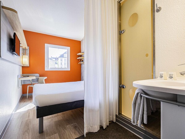 Een hotelkamer met een bed, een bureau, een badkamer met wastafel en een douche.