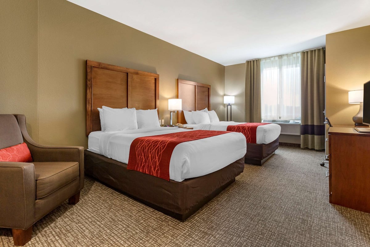 Une chambre d’hôtel avec deux lits, un bureau, une chaise et une fenêtre avec des rideaux.