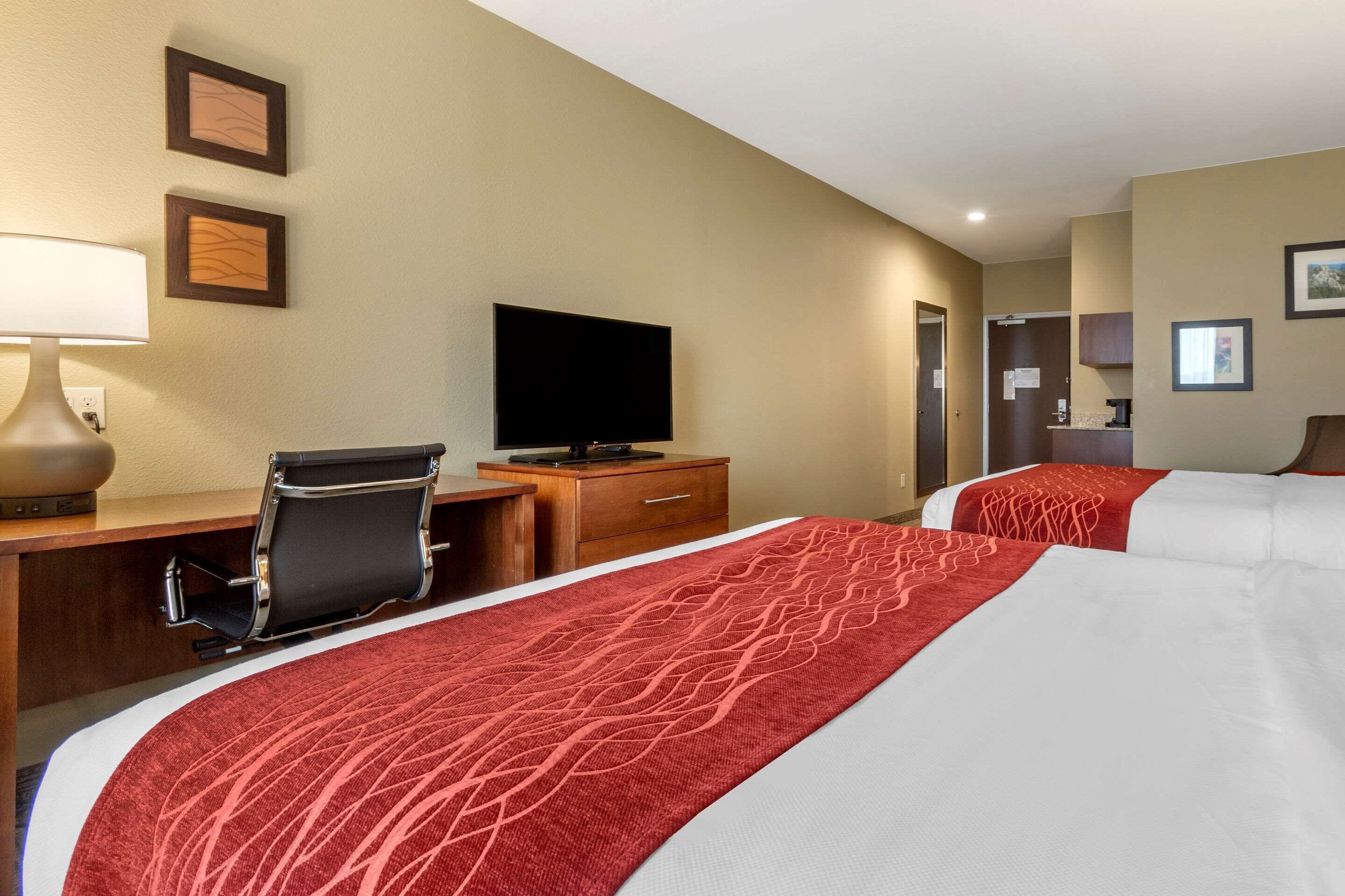 A hotel room with two beds, a desk with a chair, a television, and a mirror.