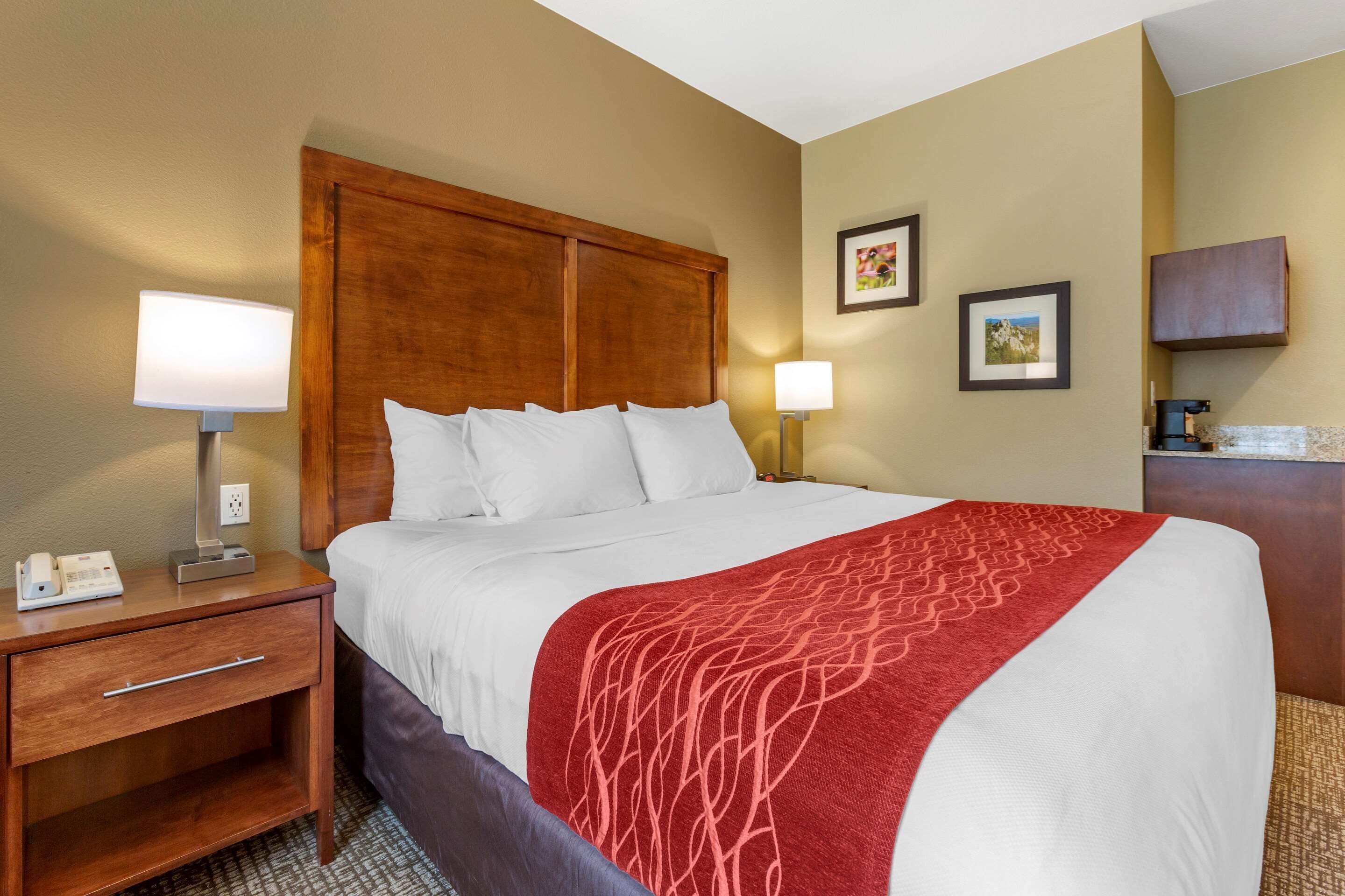 A hotel room with a large bed, two bedside lamps, a wooden nightstand, a desk, and a small cabinet.