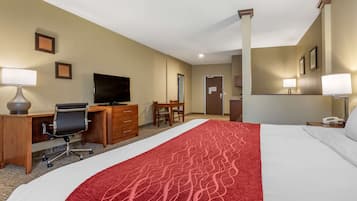 A hotel room with a large bed, a desk with a chair, a television, and a desk lamp.