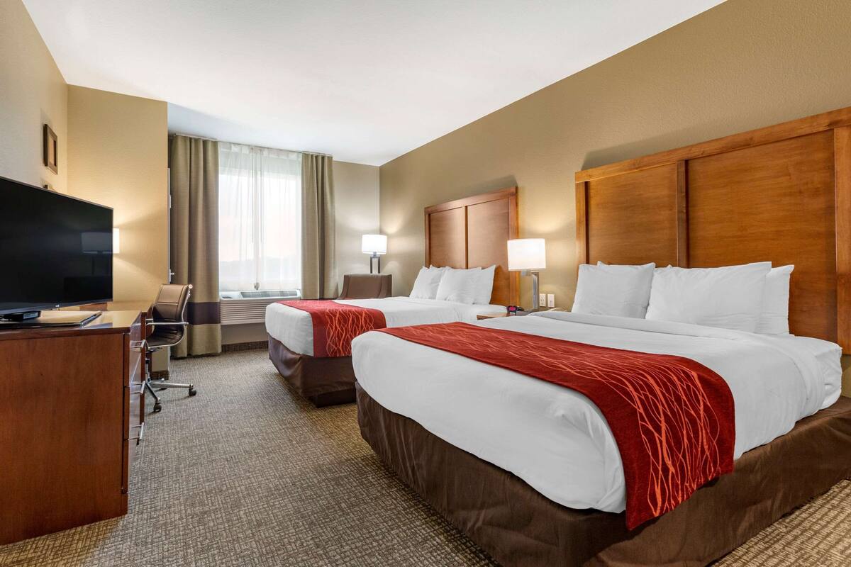 Une chambre d’hôtel avec deux lits, un bureau avec une télévision et une fenêtre avec des rideaux.