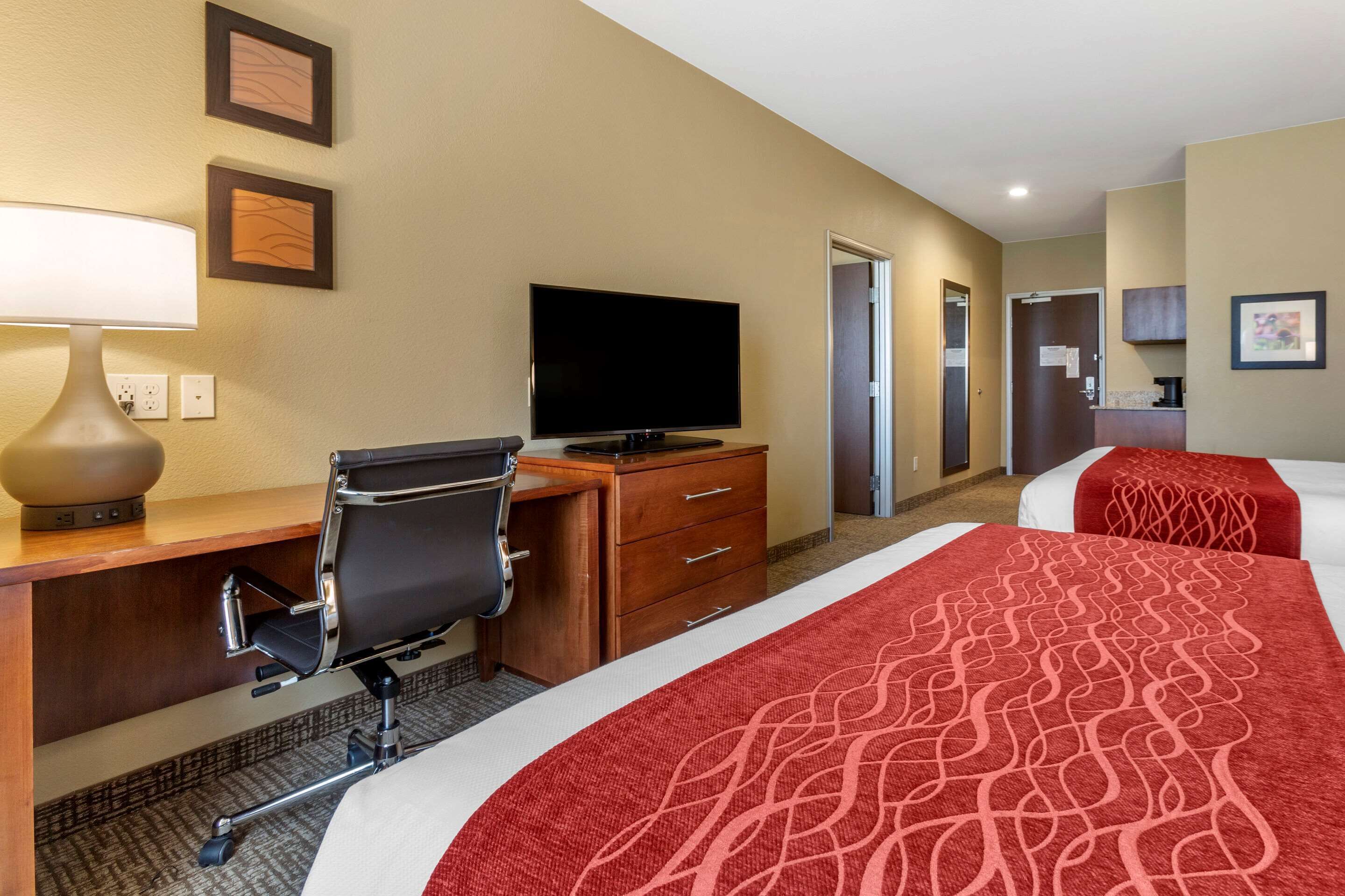 A hotel room with a desk, chair, television, and two beds with red bedding.